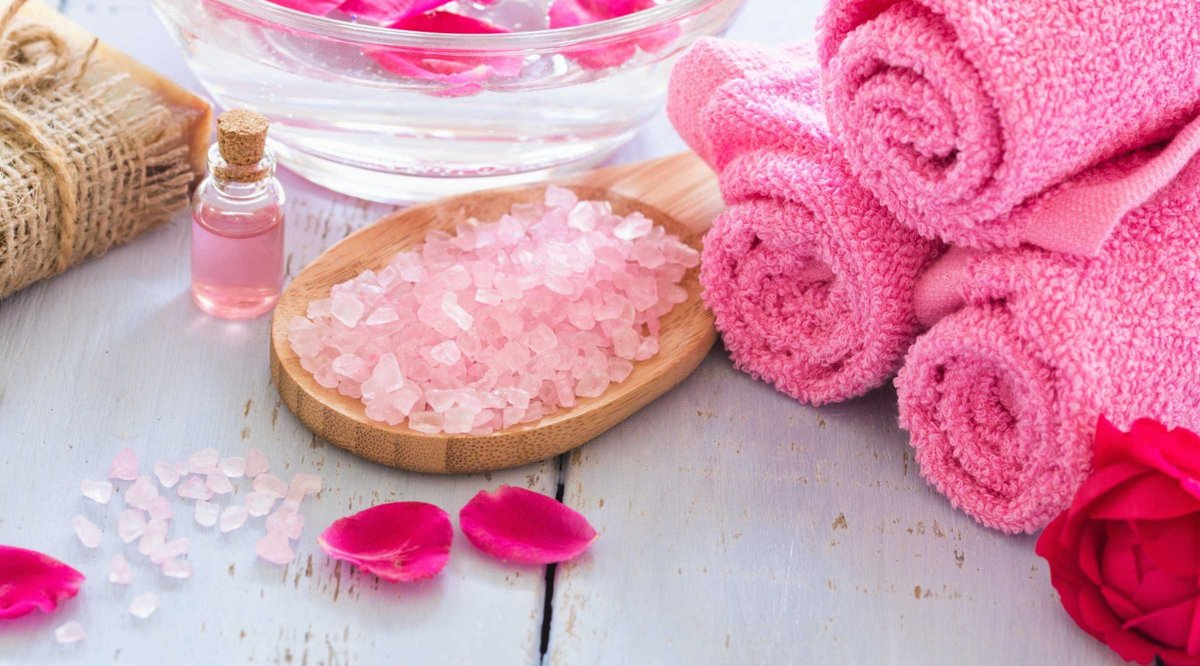 Rolled pink towels, pink bath salts and rose petals